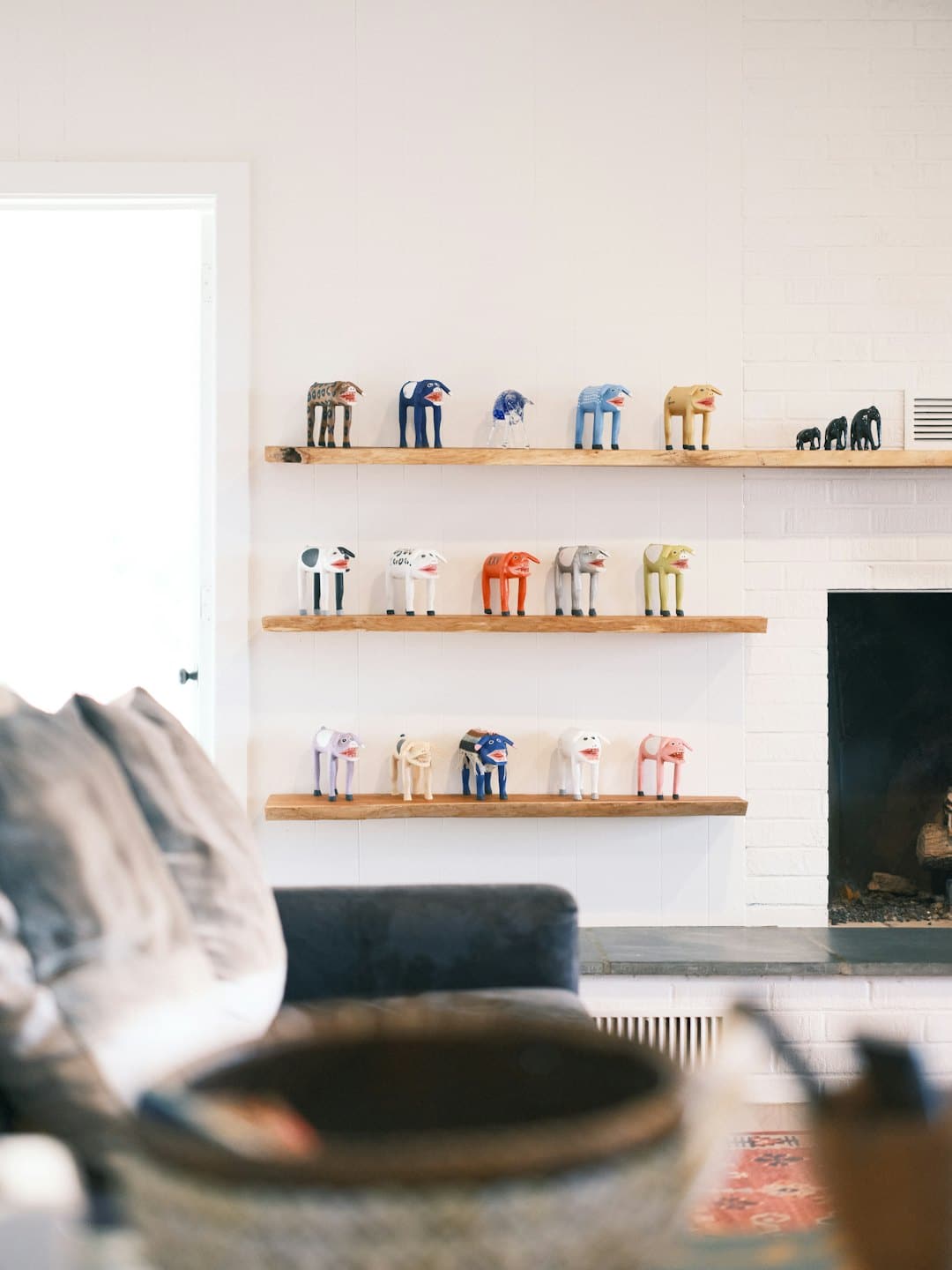 Colorful animal figurines displayed on rustic wooden shelves above a fireplace.