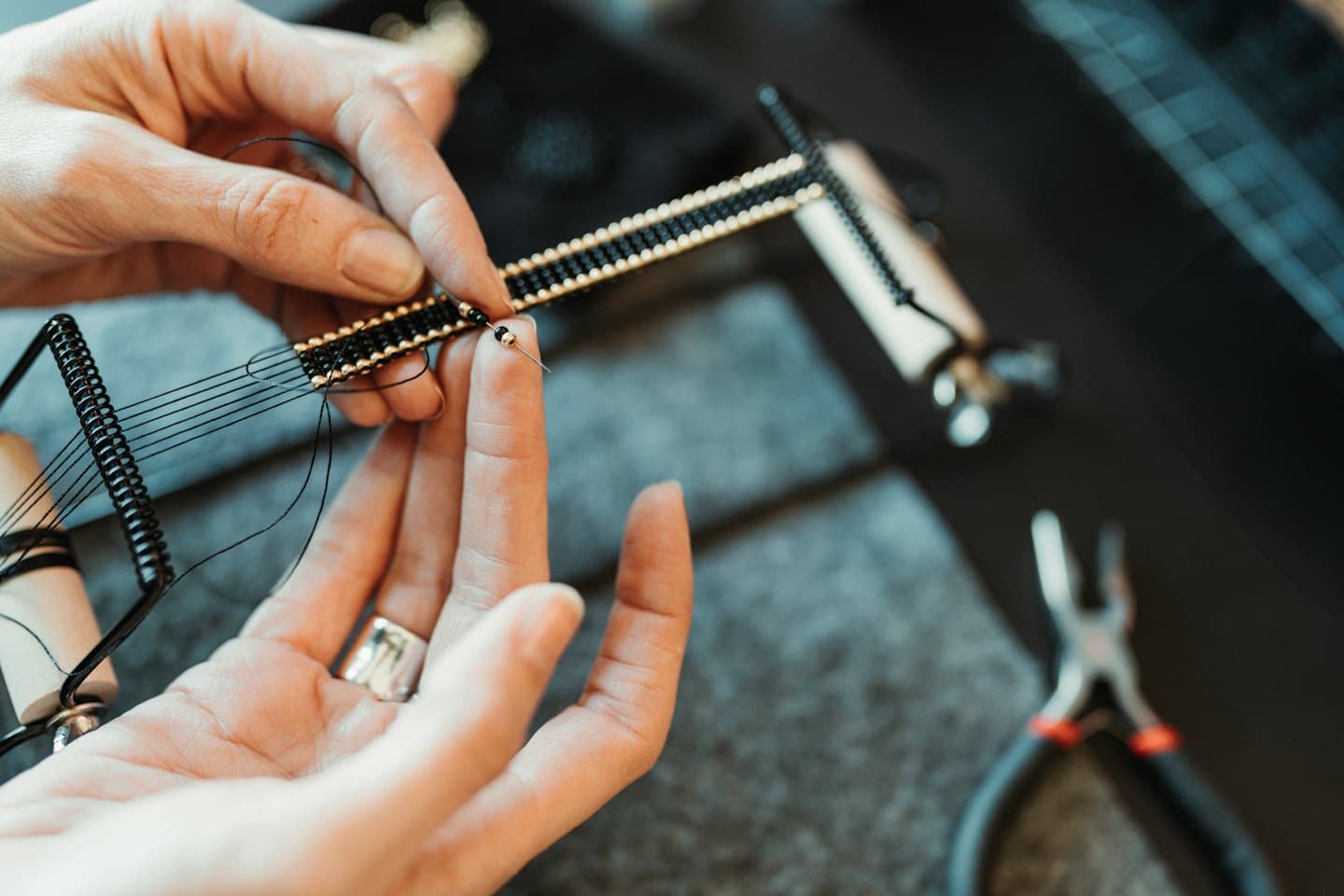 Hands weaving a black and gold beaded bracelet on a loom.
