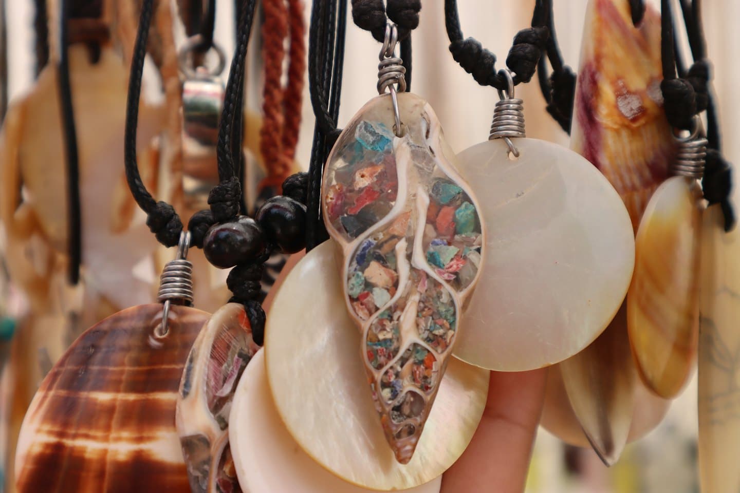 Hand holding shell necklaces with polished shells and stone inlay.
