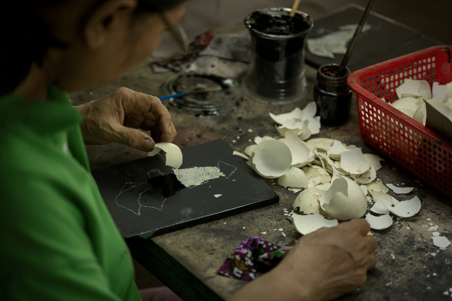Artisan carefully places eggshell pieces onto a black surface.