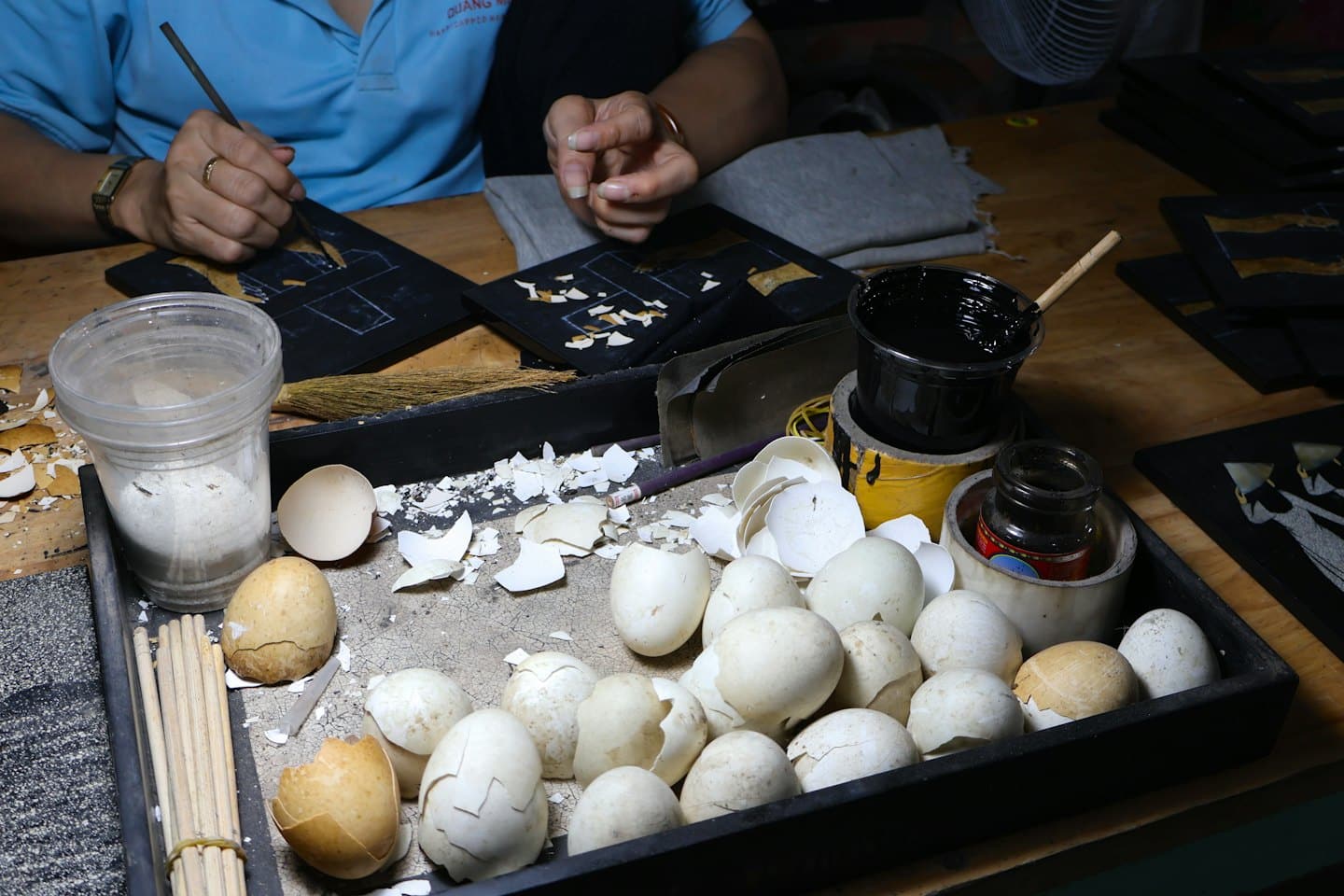 Artisan carefully places eggshell pieces onto a black board.